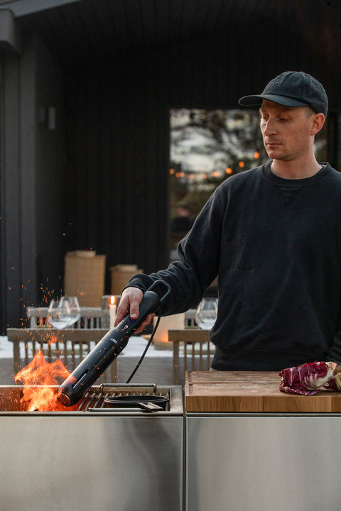 Person grilling outdoors using a Looftlighter with a wooden cutting board and meat on a grill.